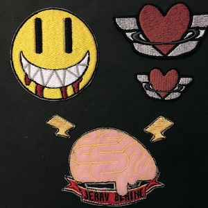 May include: Four embroidered iron-on patches. One is a yellow smiley face with red dripping blood, another is a pink brain with the text "Jerry & Shine", and the last two are red hearts with wings.