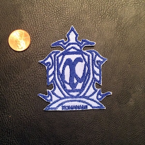 Op de afbeelding: Blauwe geborduurde patch met een witte achtergrond en een gestileerde letter "X" in het midden. De patch heeft een decoratieve rand en een banner onderaan met de tekst "EXTREME"