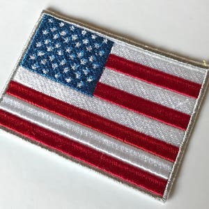 May include: A white embroidered patch with the American flag design. The flag has 13 red and white stripes and 50 blue stars on a blue field.