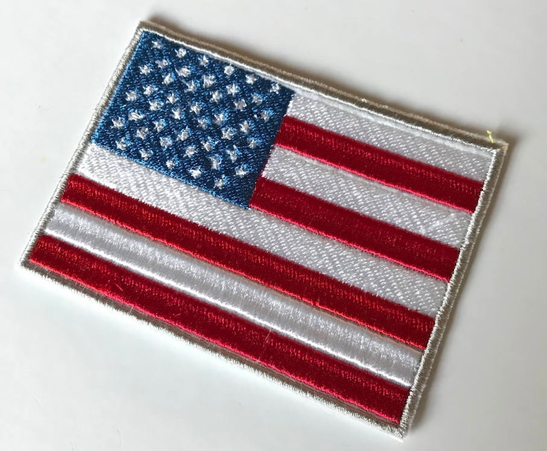May include: A white embroidered patch with the American flag design. The flag has 13 red and white stripes and 50 blue stars on a blue field.