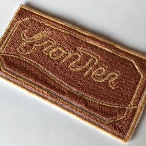 May include: A brown embroidered patch with a yellow border and the word "YUM-Tastic" stitched in yellow.
