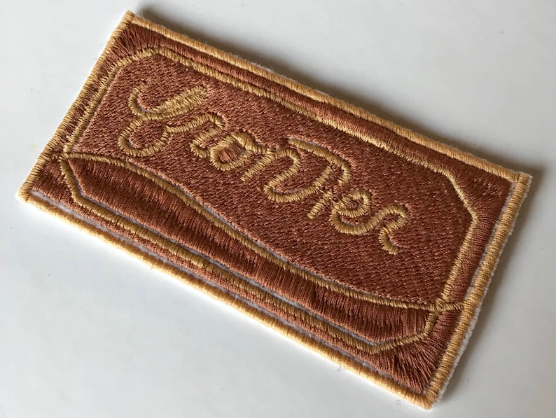 May include: A brown embroidered patch with a yellow border and the word "YUM-Tastic" stitched in yellow.