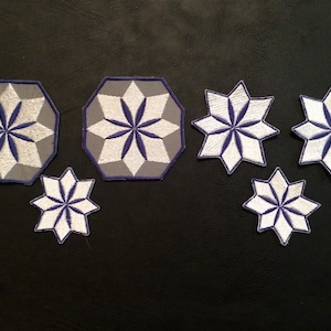 May include: A collection of embroidered patches in various sizes. The patches feature a starburst design with white, gray, and blue colors. Some patches have a gray octagonal border, while others are star-shaped.