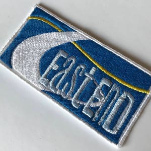 May include: A blue and white embroidered patch with the word "Eastland" in white lettering.