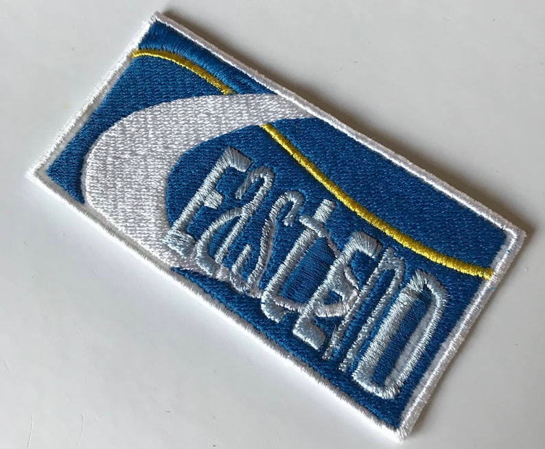 May include: A blue and white embroidered patch with the word "Eastland" in white lettering.
