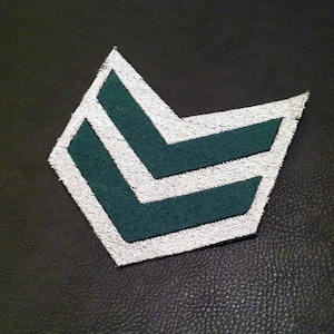 Könnte beinhalten: Ein weißer und grüner Chevron-Patch mit zwei Reihen von Chevron. Der Patch ist aus Stoff und hat einen weißen Rand.
