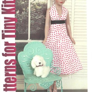 May include: A doll in a white dress with red floral print and a black belt stands next to a teal metal chair with a white stuffed dog. The image has the text "Patterns for Tiny Kitty" in a vertical red font.