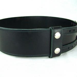 View of left side of black double buckle kilt belt. View features double snap leather keeper and detail design grooves carved in each buckle strap and along edges of belt strap and leather keeper.