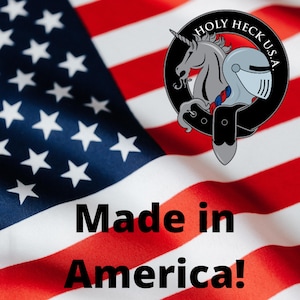 Puede incluir: Un primer plano de una bandera estadounidense doblada con las palabras "Made in America!" impresas debajo. Un logotipo en blanco y negro con un unicornio y un casco de caballero est&aacute; en la esquina superior derecha. El logotipo dice "Holy Heck U.S.A."