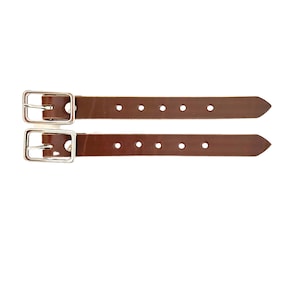 Puede incluir: Dos correas de cuero marr&oacute;n con hebillas plateadas y varios agujeros. Las correas tienen aproximadamente 2,5 cm de ancho.