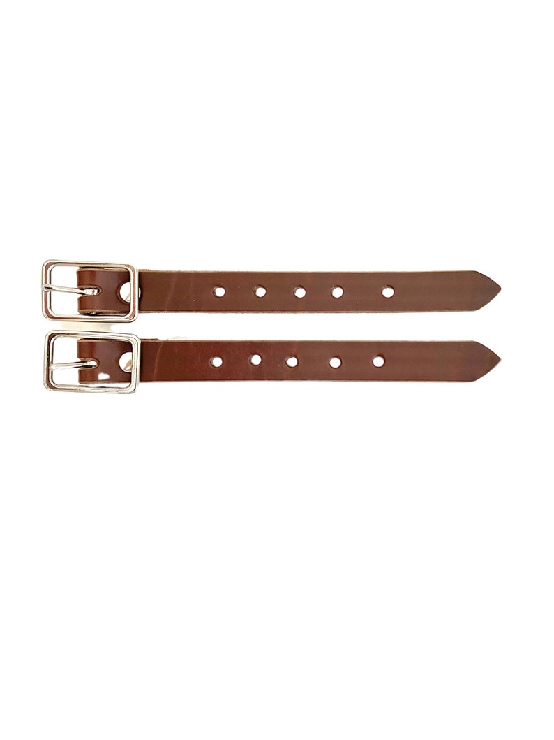 Puede incluir: Dos correas de cuero marr&oacute;n con hebillas plateadas y varios agujeros. Las correas tienen aproximadamente 2,5 cm de ancho.