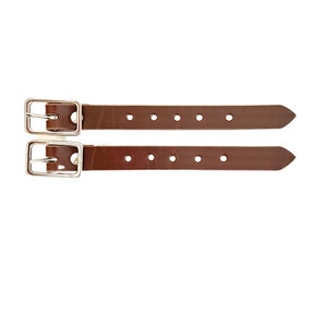 Puede incluir: Dos correas de cuero marr&oacute;n con hebillas plateadas y varios agujeros. Las correas tienen aproximadamente 2,5 cm de ancho.