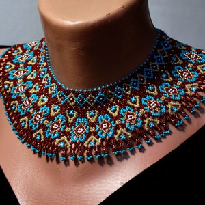 May include: A beaded choker necklace with a geometric pattern in shades of brown, turquoise, and cream. The necklace has a fringe detail.
