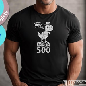 以下が含まれることがあります： 白いピクセル化された帽子をかぶった恐竜が「MOO」と書かれた吹き出しを持っている黒いTシャツ。恐竜の下には「INTERNAL ERROR 500」というテキストがあります。