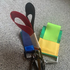 May include: Two keychains with black metal clasps. One keychain has a red, white, and blue ribbon. The other keychain has a green and yellow ribbon.
