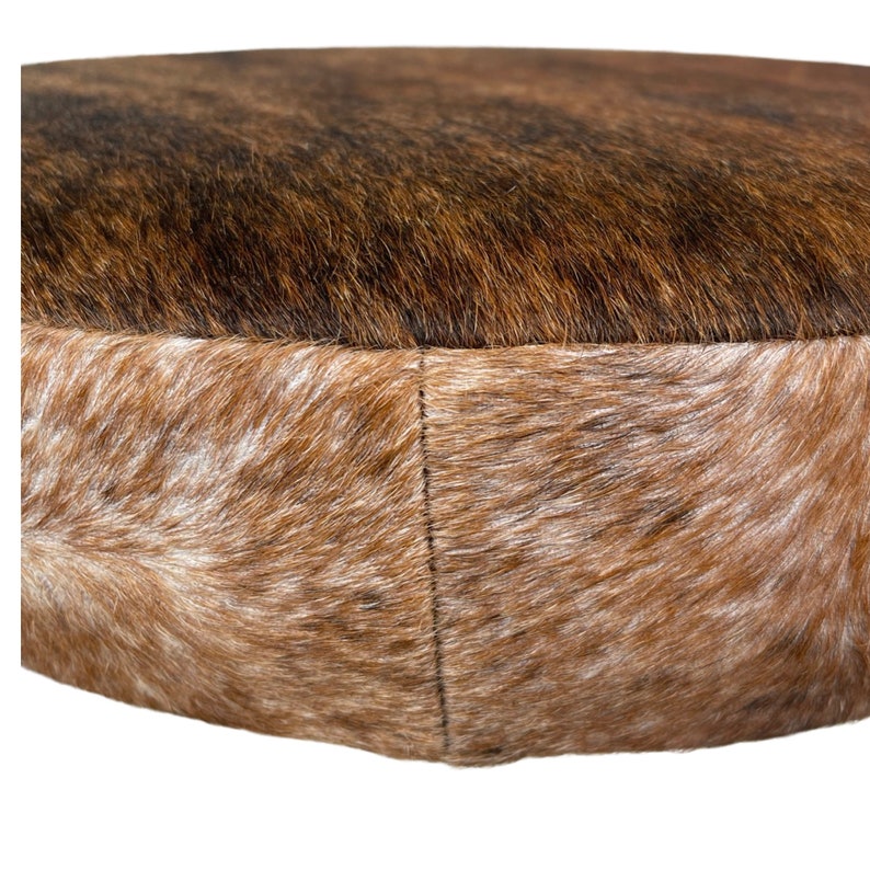 May include: A round brown and white cowhide ottoman with a stitched seam around the edge.