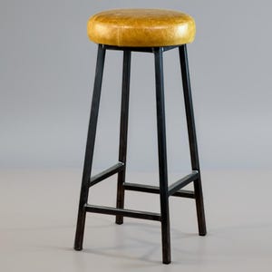 May include: A tall bar stool with a round, yellow leather seat. The stool has a black metal frame with four legs and a footrest. The seat is approximately 14 inches in diameter.