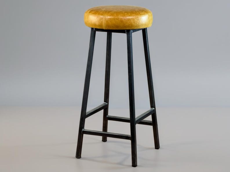 May include: A tall bar stool with a round, yellow leather seat. The stool has a black metal frame with four legs and a footrest. The seat is approximately 14 inches in diameter.