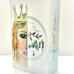 May include: A tarot card box with a watercolor illustration. The left side features a woman's face with a crown. The right side has a circular design with birds and the text "By The Way...." and "Tarot".