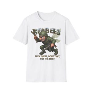 Può includere: Una t-shirt bianca con la grafica di un soldato dei cartoni animati con le ali, che tiene in mano una chiave inglese e un fucile. Il testo SEABEES è stampato sopra il personaggio, e il testo BEEN THERE, DONE THAT, GOT THE SHIRT è sotto.
