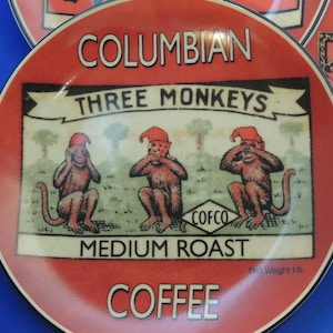 May include: A red and white ceramic coffee mug with a vintage design featuring three monkeys covering their eyes, ears, and mouth. The text "Columbian Three Monkeys Medium Roast Coffee" is printed on the mug.