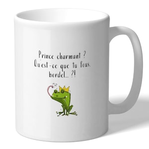 Peut inclure: Un mug en céramique blanche illustré d'une grenouille verte portant une couronne jaune avec la langue tirée. Au-dessus de la grenouille, le texte indique : Prince charmant ? Qu'est-ce que tu fous, bordel... ?!