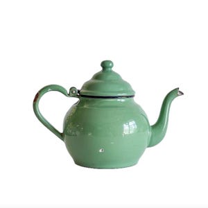 May include: A vintage, light green enamel teapot with a curved handle and spout. The teapot has a matching lid and a black trim around the base and lid. The teapot shows signs of wear, adding to its antique charm.