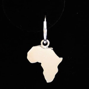 May include: A silver earring in the shape of the African continent. The earring is suspended from a small hoop. The design is simple and elegant. The earring is set against a black backdrop.
