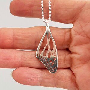 May include: Silver necklace with a delicate butterfly wing pendant. The pendant is made of a thin, openwork design with a detailed pattern.