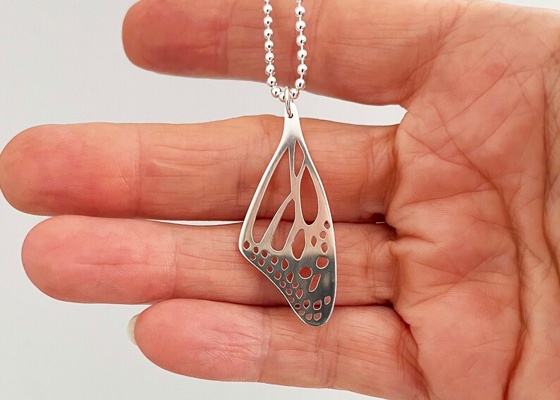 May include: Silver necklace with a delicate butterfly wing pendant. The pendant is made of a thin, openwork design with a detailed pattern.