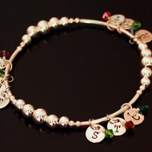 May include: Silver charm bracelet with silver beads and charms with letters D, T, S, and N. The charms are accented with green and red gemstones.