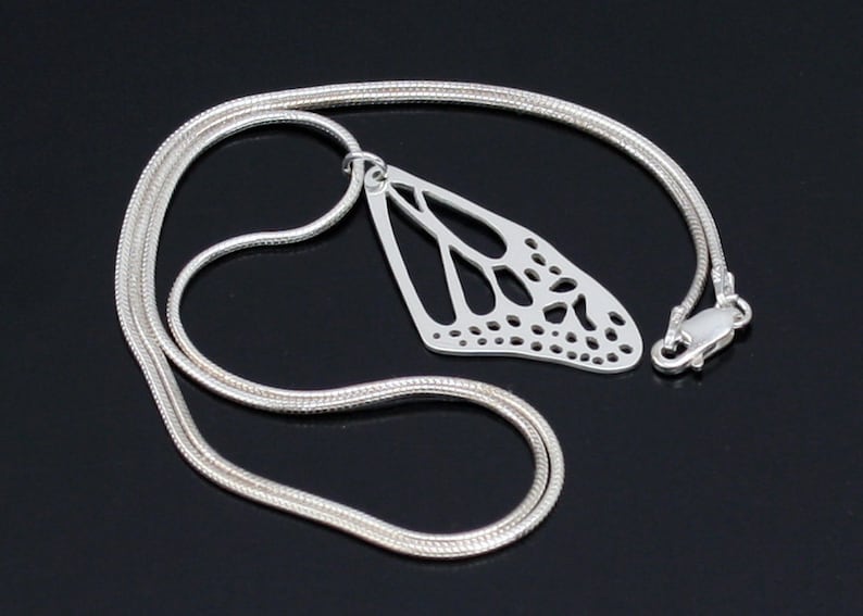 May include: A silver chain necklace with a delicate, cutout butterfly pendant. The pendant is detailed with intricate lines and small circles.