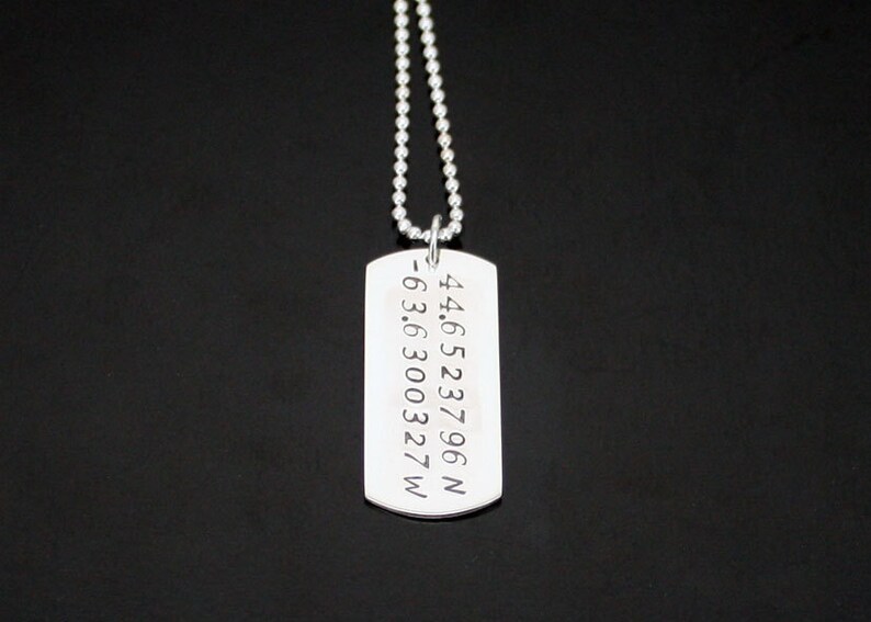 May include: Silver necklace with a dog tag pendant engraved with the coordinates 44.6523796 N -63.6300327 W.