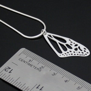 May include: Silver necklace with a delicate butterfly pendant. The pendant is made of a single wing with a detailed, intricate design. The necklace is 1.75 inches long.