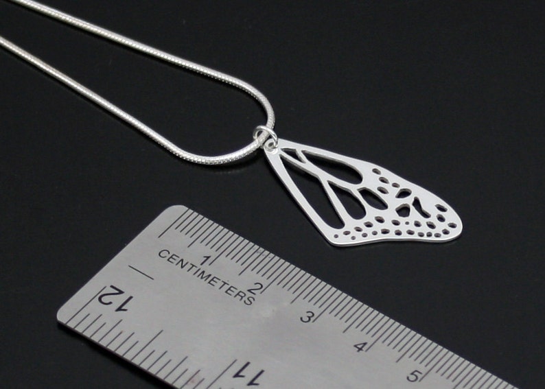 May include: Silver necklace with a delicate butterfly pendant. The pendant is made of a single wing with a detailed, intricate design. The necklace is 1.75 inches long.