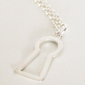 May include: A silver-colored keyhole pendant necklace. The pendant is a stylized keyhole shape with a rounded top and a rectangular base. The necklace chain is a delicate silver ball chain.