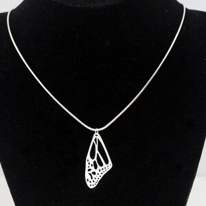 May include: A silver chain necklace with a delicate butterfly pendant. The pendant is cut out in the shape of a butterfly wing, creating a delicate and intricate design.