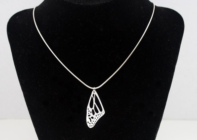 May include: A silver chain necklace with a delicate butterfly pendant. The pendant is cut out in the shape of a butterfly wing, creating a delicate and intricate design.