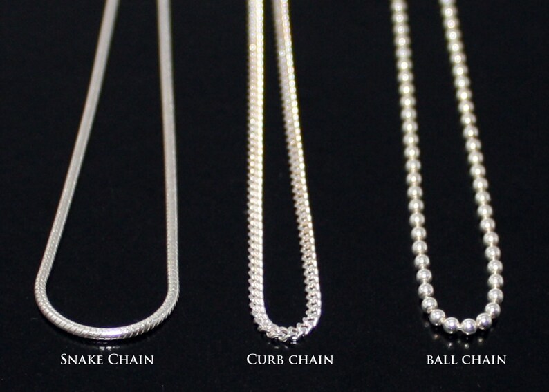May include: Three silver chains, a snake chain, a curb chain, and a ball chain, are displayed against a black background. The chains are all the same length and are hanging straight down.