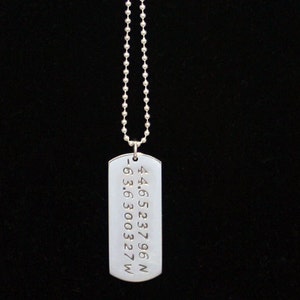May include: Silver necklace with a dog tag pendant engraved with coordinates: 44.6523796 N -63.630327 W