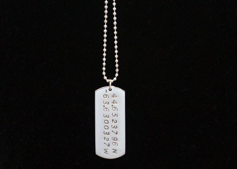 May include: Silver necklace with a dog tag pendant engraved with coordinates: 44.6523796 N -63.630327 W
