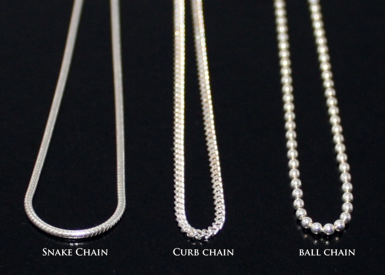 May include: Three silver chains, a snake chain, a curb chain, and a ball chain, are displayed against a black background. The chains are all the same length and are hanging straight down.
