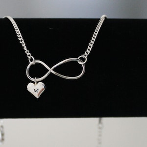 May include: Silver infinity necklace with a small heart charm engraved with the letter "M".