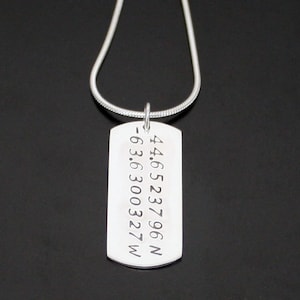 May include: Silver necklace with a dog tag pendant engraved with the coordinates 44.6523796N -63.6300327W.