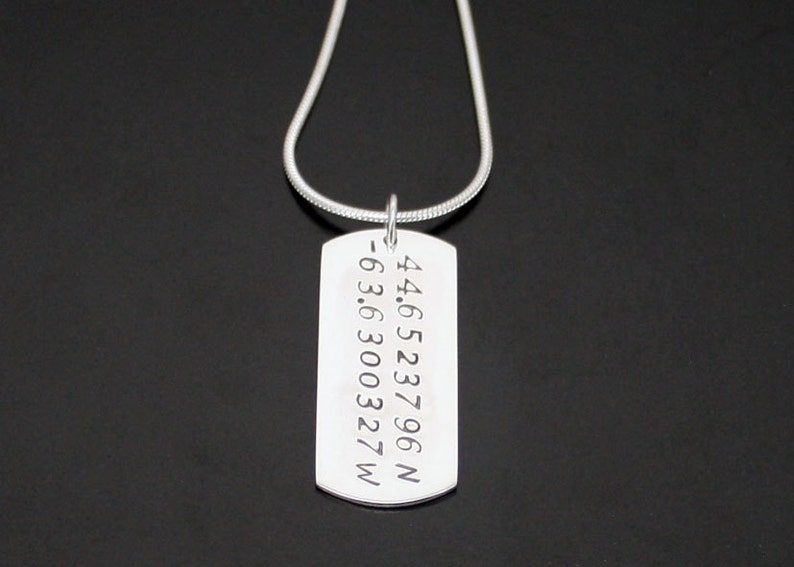 May include: Silver necklace with a dog tag pendant engraved with the coordinates 44.6523796N -63.6300327W.