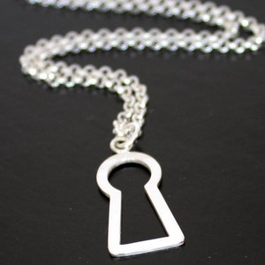 May include: A silver-colored necklace featuring a keyhole pendant. The pendant is a simple, open keyhole shape, and the chain is a delicate, linked design. The necklace is displayed against a dark background.
