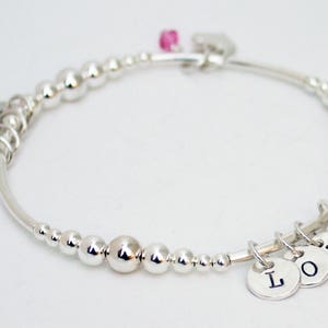 Può includere: Braccialetto in argento con un ciondolo rosa e cinque ciondoli in argento che compongono la parola "LOVE".