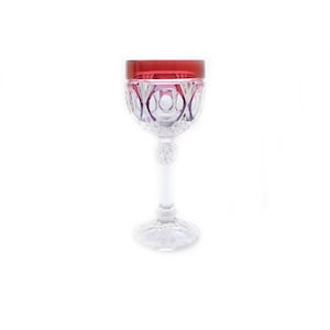May include: A clear glass wine goblet with a cut crystal design. The goblet has a red rim and a tall stem.