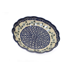 May include: A large, white ceramic serving bowl with a blue and white woven pattern and a blue floral border. The bowl has a scalloped edge.