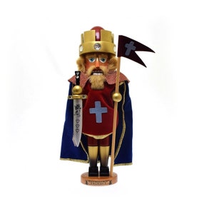 May include: A wooden nutcracker figurine of a king wearing a gold crown, red and blue robes, and holding a sword and a flag with a cross. The base of the nutcracker reads "King Richard II".